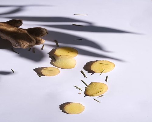 Thickly sliced raw ginger roots resting next to a white ceramic pouring teapot