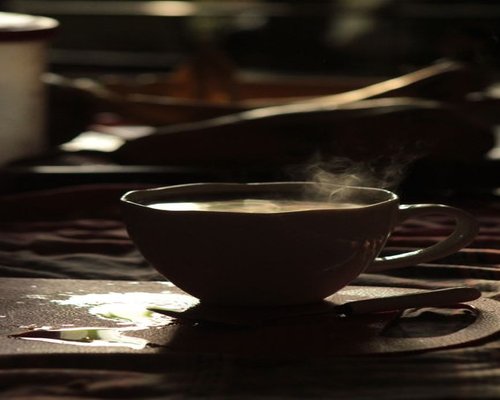 A warm steaming mug of home brewed lemongrass infusion resting on a rustic wooden table during sunset