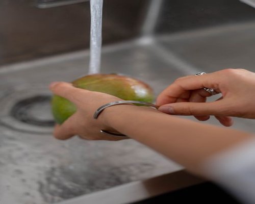 A pristine stainless steel bowl filled with fresh water washing deep green spinach leaves and ripe mangoes